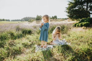 Child portrait session with two sisters examining dandelion flowers in the grass taken at Helvetia Lavender Farm near Hillsboro and Portland Oregon.