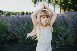 Child portrait session with young girl swinging her blonde hair in front of a lavender bush taken at Helvetia Lavender Farm near Hillsboro and Portland Oregon.