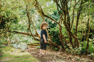 Child looks pensively over his shoulder next to some trees.