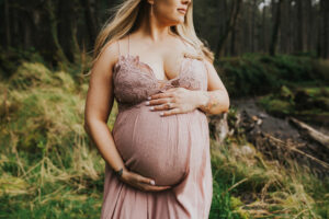 Close up on the bump of a pregnant woman in a pink dress during her maternity photo session on the Oregon Coast with Meg Ross Photography