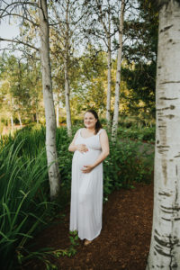 Pregnant mom smiles in the middle of some trees in Hillsboro, Oregon.
