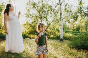 Toddler daughter blows dandelion wishes during a maternity session in Hillsboro, Oregon.