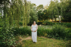 Pregnant mom smiles in the middle of a park full of greenery in Hillsboro, Oregon.Grass