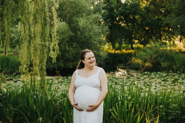 Close up as pregnant mom smiles in the middle of a park full of greenery in Hillsboro, Oregon.Grass