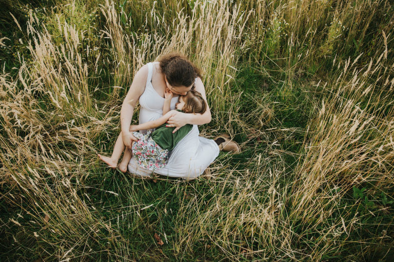 Pregnant mom tickles and snuggles her oldest daughter thinking about pregnancy the second time around in the tall grass in Hillsboro, Oregon