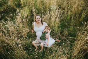 Pregnant mom tickles and snuggles her oldest daughter thinking about pregnancy the second time around in the tall grass in Hillsboro, Oregon