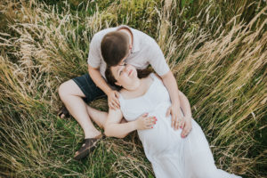 Pregnant mom, dad/partner, and oldest daughter snuggle and tickles in the grass during their maternity session in Hillsboro, Oregon