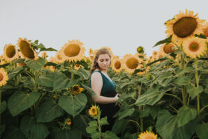 Sideview of a pregnant women holding her maternity bump and looking down her shoulder in a sunflower field in Hillsboro Oregon during her maternity photo session