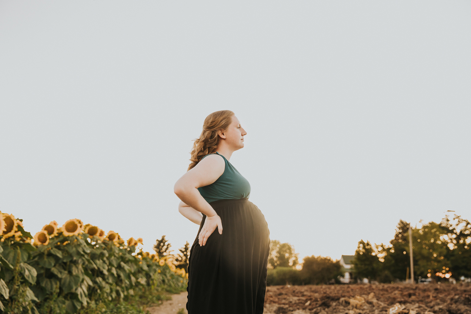 Pregnant mom's body is pointed to the right with her bump framed against the sky at West Union Gardens in Hillsboro Oregon during a maternity photo session.