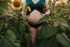Peekabo glimpse at a bare pregnant belly framed by sunflowers at West Union Gardens in Hillsboro Oregon during a maternity photo session.