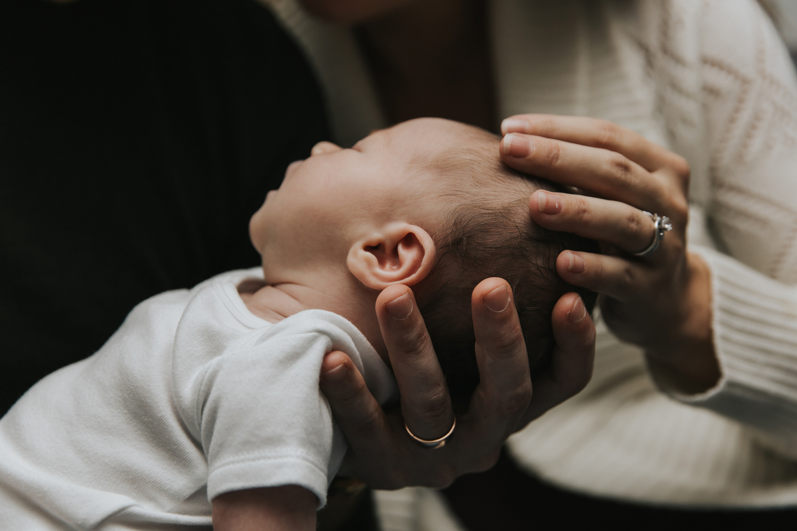 Close up on mom and dad's hands cradling baby's head during lifestyle newborn session by Portland Newborn Photographer.