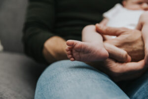 Close up on baby's foot while sitting in dad's lap during lifestyle newborn session by Portland Newborn Photographer.
