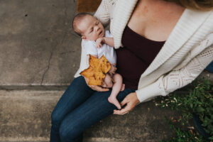 Baby held outdoors in mom's lap being covered by a large leaf during lifestyle newborn session by Portland Newborn Photographer.