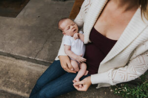 Baby held outdoors in mom's lap during lifestyle newborn session by Portland Newborn Photographer.