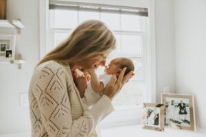 Mom and baby eskimo kiss in front of window at a lifestyle newborn session by Portland Newborn Photographer.
