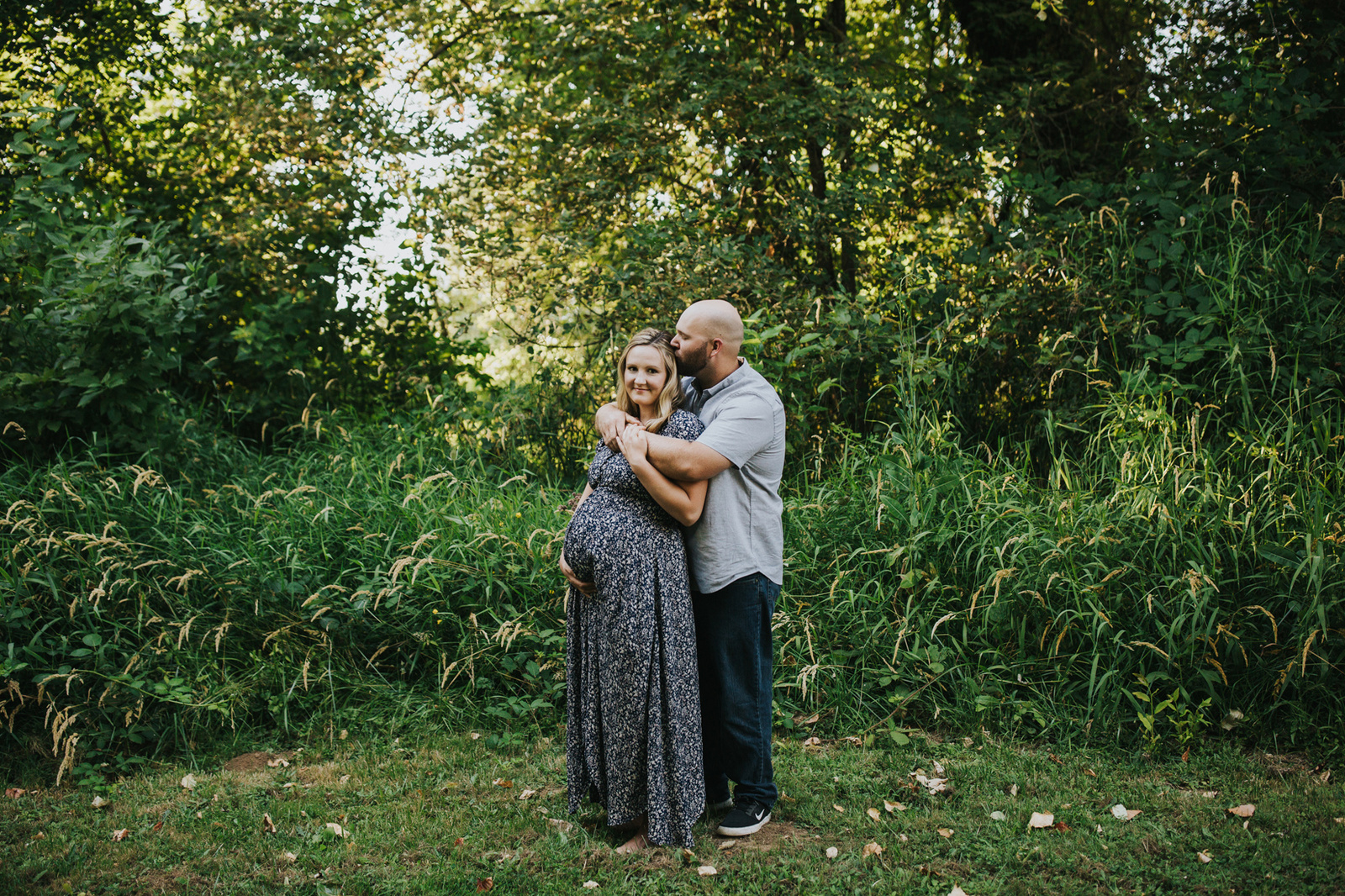 Mom looks at me while partner kisses her head on the farm during their Yamhill, OR maternity session.