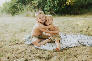Two brothers hug each other looking towards the camera while sitting on a blanket