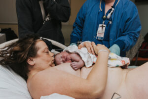 Mom wraps her arms around her skin-to-skin baby and kisses the top of his head in a Kaiser Westside delivery room.