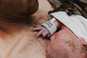 Close up of newborn baby doing skin to skin on his dad's chest while his fingers curl up in the chest hair