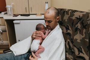 Brand new dad adjusts his position while holding his baby by the back to put him on his chest