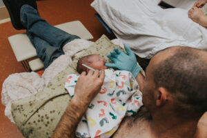 New baby is laying tummy up on a pillow while dad uses a gloved hand to feed him colostrum via syringe at Kaiser Westside in Hillsboro Oregon