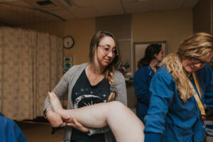 Labor doula Kendelle looks down at mom and holds one of mom's legs up high while nurses attends