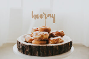 A pile of donuts on a wooden platter with a HOORAY sign sticking out at the top of the pile
